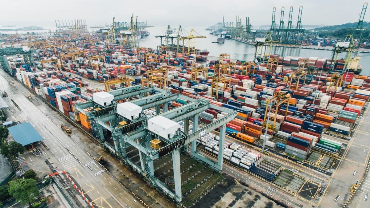 Shipping containers stacked across a freight terminal beside loading cranes